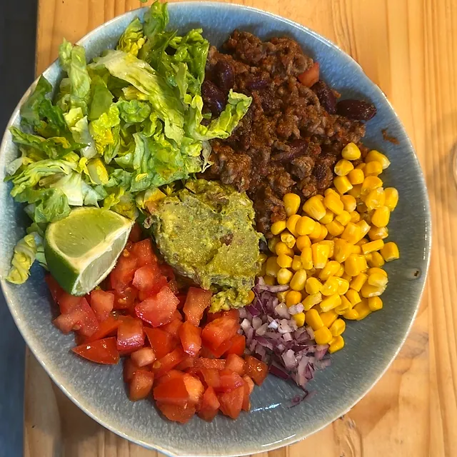 Bol de salade composée : bœuf haché, maïs, tomates en dés, laitue, guacamole et haricots rouges, photographié d'en haut.